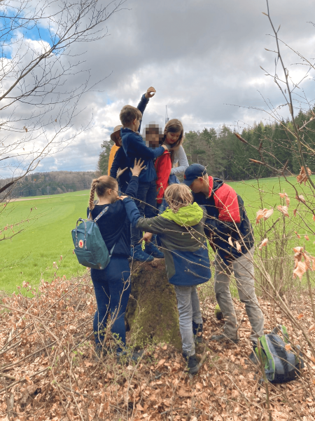Kinder und Jugendliche versuchen als Gruppe auf einen Baumstumpf zu balancieren