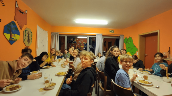 Kinder, Jugendliche und Leiter essen Nudeln im Gruppenraum